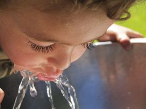 Little boy leaning into with lips in water spurt of drinking  fountain.