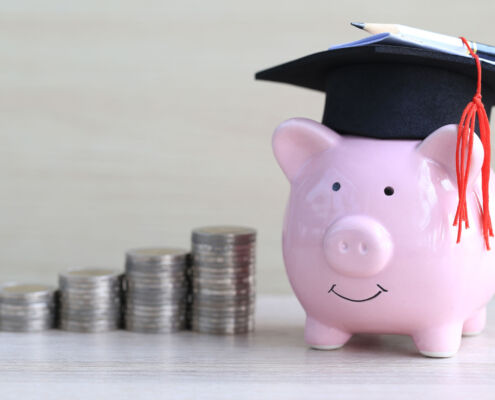 Graduation hat on pink piggy bank with stack of coins money on wooden background, Saving money for education concept Bildung Ausbildung Kosten Sparschwein Investition
