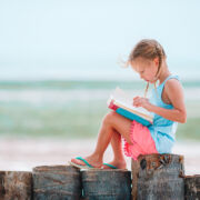 Little adorable girl reading book during tropical white beach